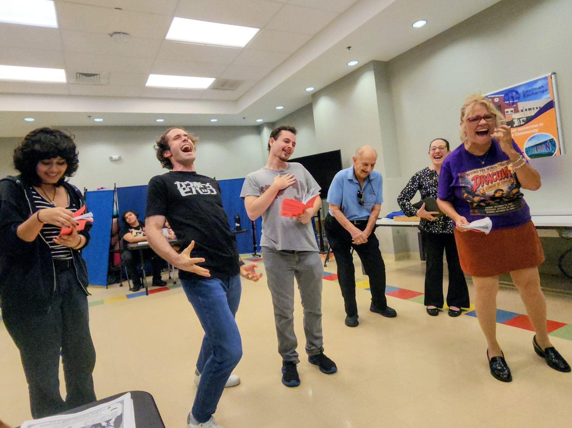 Beyond the Wings Theater cast members laugh during a Dracula: A Comedy of Terrors rehearsal at the Lealman Exchange, one wearing a purple Dracula show t-shirt.